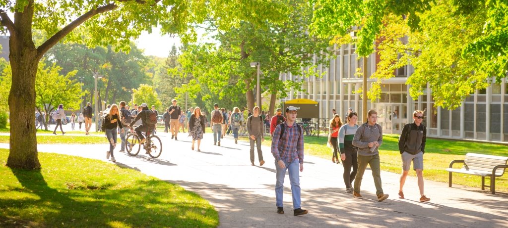 Students walking and biking between classes on the Michigan Tech campus in spring with trees in bloom.