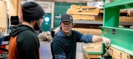 Two students with glasses in the Boardsports Technology Enterprise woodshop.