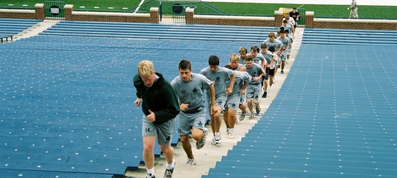 A coach leads his team up the steps on a stadium run.