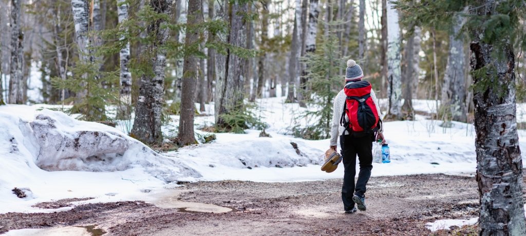 Students in the new nature psychology course capped off spring semester by putting what they learned into practice at Porcupine Mountains Wilderness State Park. A young woman with a backpack and her back to us carries her snow boots and water on a trail back to a nature psychology exploration in a wilderness park.