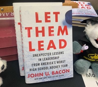 The book Let Them Lead by John Bacon next to a fuzzy Husky in the MTU Bookstore