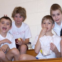 Four little boys on a basketball team clown in the stands in a gym in 2007.
