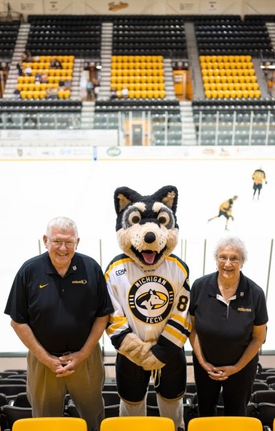 A couple in Michigan Tech shirts who supports the mascot program pose with Blizzard T. Husky at the ice arena.