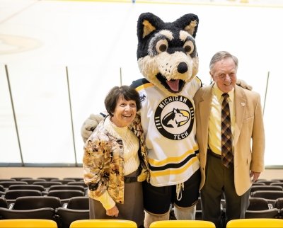 The original MTU mascots pose with Blizzard T. Husky in Michigan Tech's hockey rink in the bleachers.