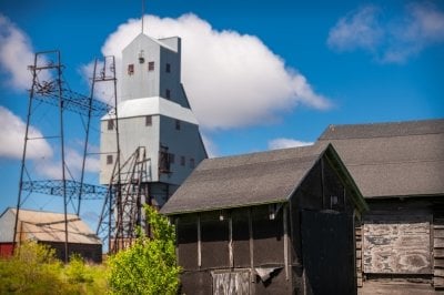 The Quincy Hoist and Shafthouse under a blue sky with the remnants of mining housing and storage in the foreground as researchers consider new ways to use old mines to empower community with electricity and agency.