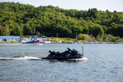 A wave-running jet ski-style autonomous vehicle maneuvers on the Keweenaw waterway next to the Isle Royale seaplane with a marina in the background near Michigan Tech's Great Lakes Research Center