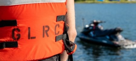 A life jacket reads GLRC for Great Lakes Research Center with an autonomous wave runner in the water in the background as Michigan Tech gears up for the Smart Ships Coalition workshop in September 2022.