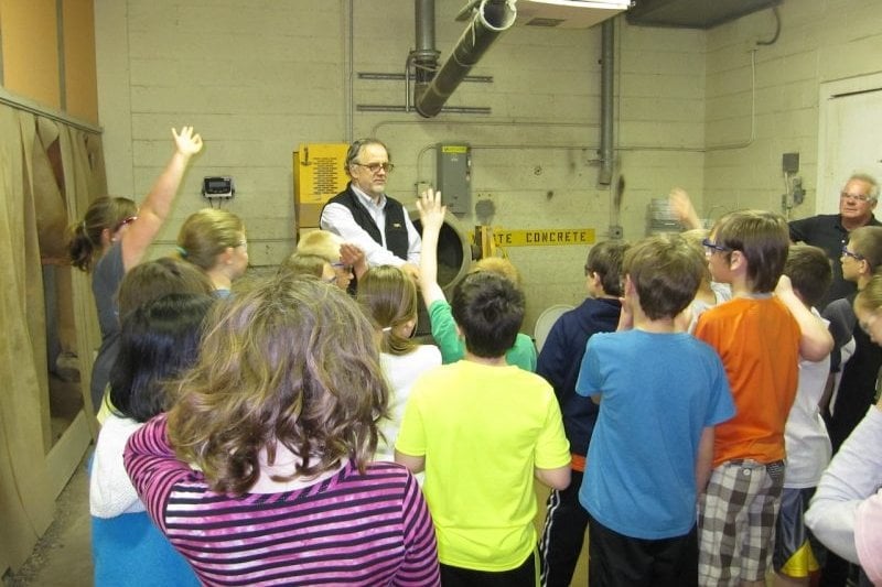 Having fun in the lab with excited young students. Larry standing with a group of young students, some with hands raised.