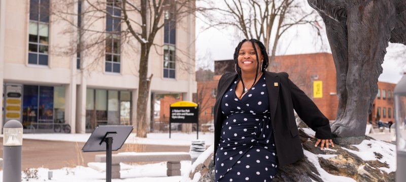 A young woman stands next to the Husky statue smiling outside with snow on the ground, she is graduation speaker