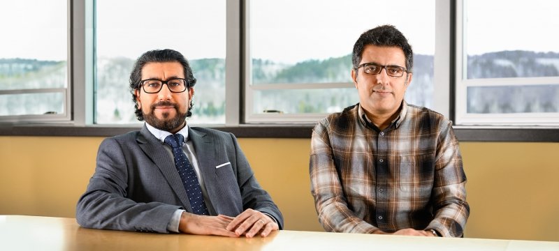 Two researchers sit at a conference table with a snow-capped hillside outdoors in the background at Michigan Technological University, where they have recently won prestigious CAREER Awards.