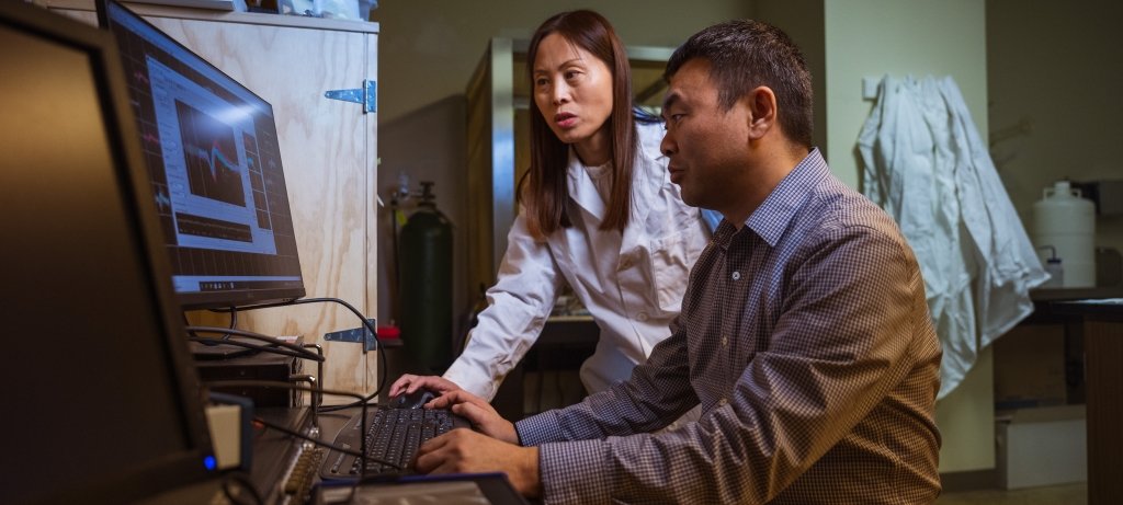 Two Michigan Tech researchers confer in front of a computer screen in a lab where they are working to improve deep brain stimulation systems.