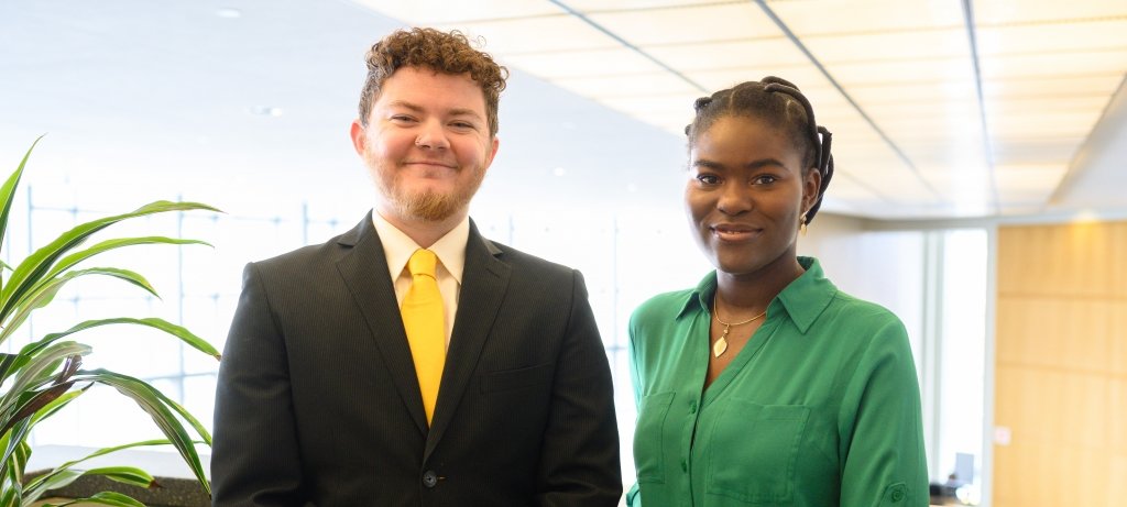 Two students speaking at spring commencement at Michigan Tech smile on a balcony overlooking the library.