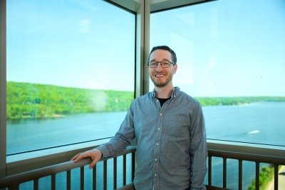A smiling researcher with the Keweenaw waterway behind him in the hall outside his biological sciences research lab at Michigan Tech.
