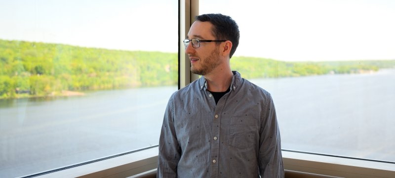 A researcher smiles in the foreground framed by the Keweenaw Waterway in the biological sciences department of Michigan Technological University.