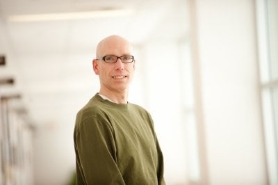 A senior design team advisor for materials science and engineering at Michigan Tech is shown in a portrait in a light-filled hallway in his building.