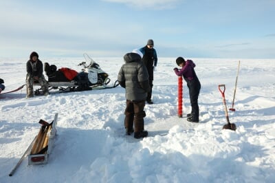 Researcher turning an ice drill by hand while others watch.