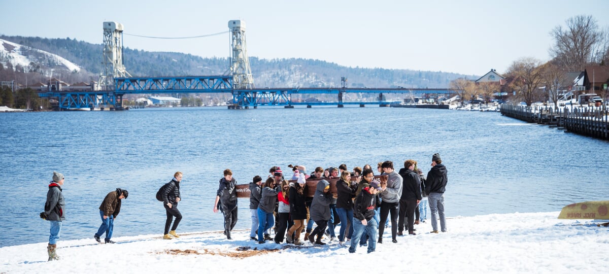 From April 10-12, Michigan Tech welcomed over 400 civil engineering students from universities across Michigan and Ohio to Houghton for the annual Eastern Great Lakes Student Symposium. Students carry a concrete canoe from the snowy banks of the Keweenaw Waterway with the Portage Lift Bridge in the background.