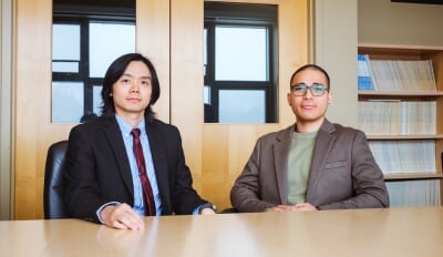 Xue, left, wears a black blazer, blue striped shirt, and red tie next to Kayastha, wearing a brown blazer and green shirt.