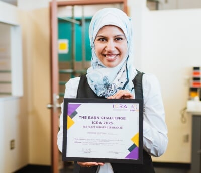 Amna Mazen poses with her BARN Challenge certificate that reads 'The BARN Challenge, ICRA 2025, First Place Winner Certificate'