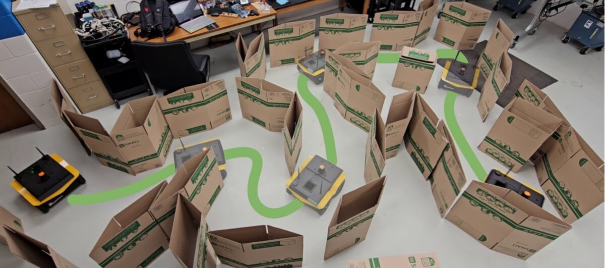 A challenge environment is laid out using cardboard boxes. A green graphic line shows the successful path for the robot to navigate.
