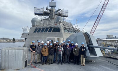 Michigan Tech ASME students pose in a group shot aboard a Marinette Marine-produced naval vessel, all wearing hard hats.