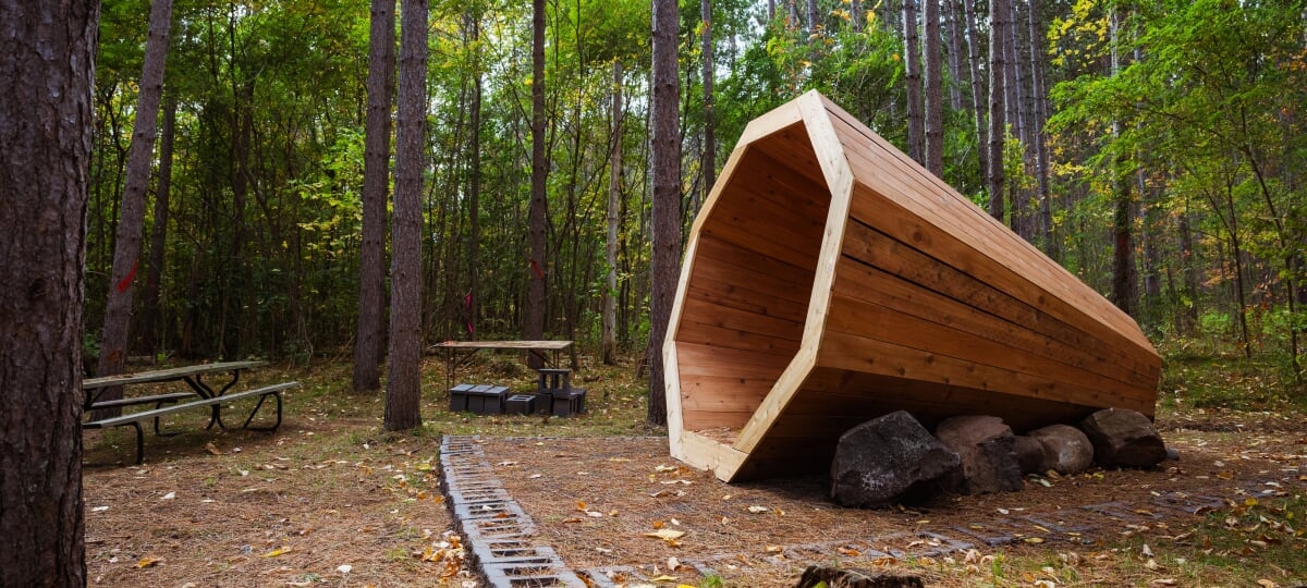 This nature megaphone–a new addition to the Tech Trails–offers visitors a quiet place to sit in contemplation and hear the subtle ambiance of nature. A large conical, megaphone shaped, wooden structure in the woods.