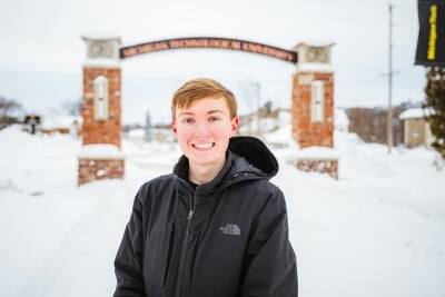Andrew Hemstreet sands in front of the Alumni Gateway arch in the winter.