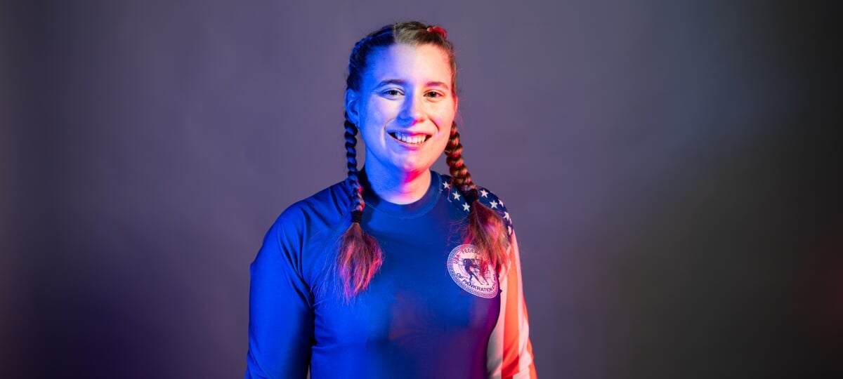 Haley Peterson’s achievements in the sport of pankration took her from Michigan’s Upper Peninsula to Greece and Romania. Now, she’s back in the U.P. as a proud Michigan Tech Husky. Haley Peterson wears her official pankration jersey in front of a dark studio backdrop.