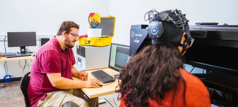 A participant wearing motion-tracking equipment plays a computer game in a lab while sensors record hand movements.