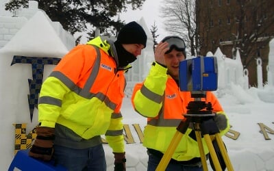 Students in a surveying club stand near large snow statues during Michigan Tech Winter Carnival taking lidar scans of the structures.