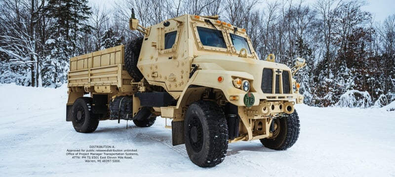 A large, tan-colored tactical vehicle stands parked outside in the snow.