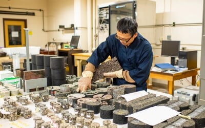 Zhanping You examining cylindrical core samples of asphalt and concrete in a laboratory setting with testing equipment.