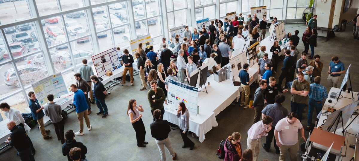 Michigan Tech’s Enterprise Program is continuing to expand its offerings with three new teams in the last two years: Aeronautics and Rocketry, Urban Intelligence Lab, and Ink & Ore. Large group of people attending an academic poster presentation in a spacious, sunlit hall with floor-to-ceiling windows.
