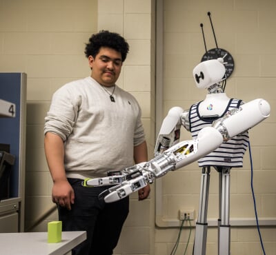 A student watches Reachy the Robot reach for a block on the table in Michigan Technological University's Human-Robot Interaction Lab.