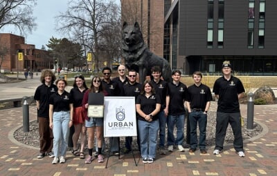 Group of Michigan Tech students standing outdoors in front of the husky statue on campusaround a sign that reads 'Urban Intelligence Design'.