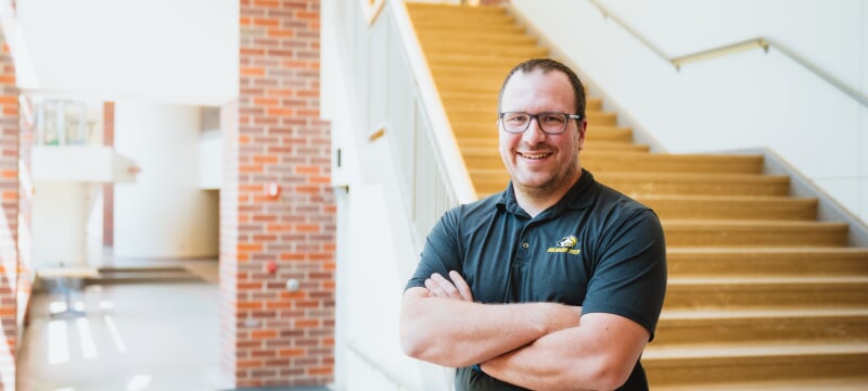 Zack Fredin stands with arms crossed in front of open staircase.