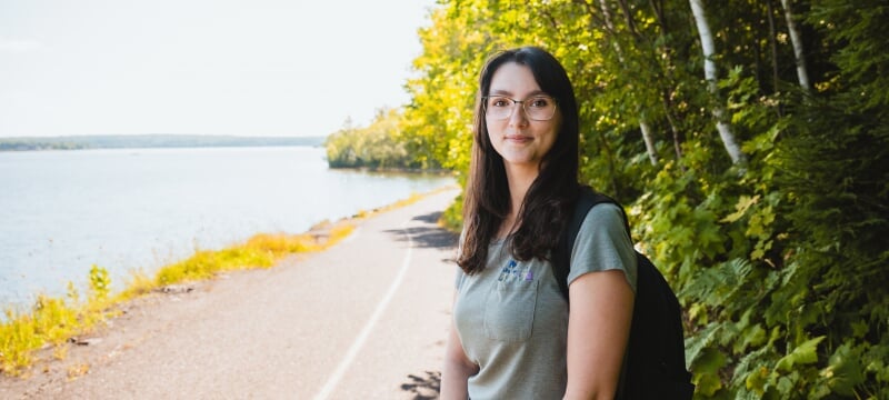 Jennifer Celeste stands with a backpack over her shoulder on a paved waterfront trail.