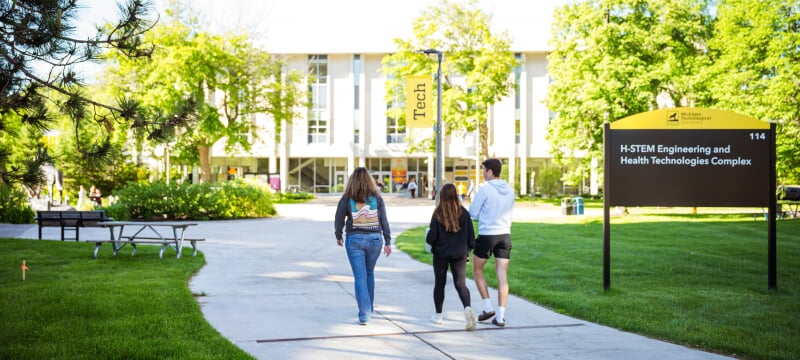 Three students walk across Michigan Tech’s campus near the H-STEM Engineering and Health Technologies Complex.