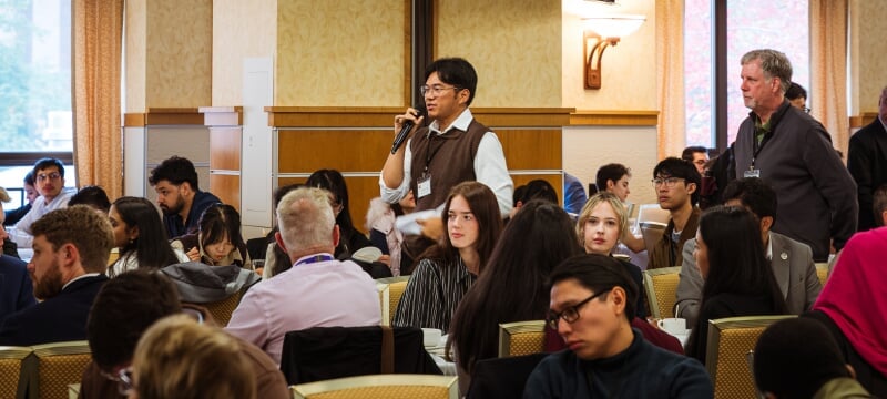 A student attending the North American Power Symposium at Michigan Tech takes part in a conversation in a ballroom setting surrounded by hundreds of other students attending the event.