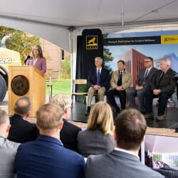 Laura Bulleit speaking at the podium while others watch from the stage.