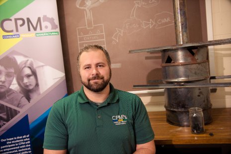 Michigan Tech senior Paul Hagadone of the Consumer Product Manufacturing Enterprise, which aims to bring clean-burning biochar to wood-fired cook stoves in Benin. A jar of biochar is pictured in front of a student-made biochar kiln. Sarah Bird photo