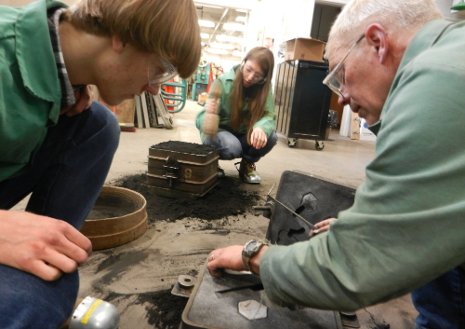 Dale Dewald, at right, and Finlandia sculpture students open a green sand mold to pull out the patterns and to cut passageways (called gates) for the metal to flow into the molded cavities.  