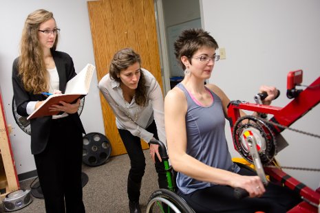Physical therapy graduate students Lydia Lytle and Jennifer Dannenbring help Samantha Schroth, Ms. Wheelchair America 2015, use a new motor-driven arm cycle as part of a multi-disciplinary research study that bridges engineering and rehabilitation.