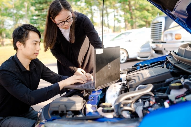 two people in front of a computer balanced on the hood of a car