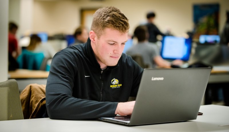 Michigan Tech student working at a computer and wearing clothing with the University’s spirit mark.