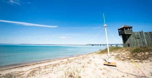 A high-frequency radar tower, which is a 14-foot tall thin metal tower with a spherical compartment near the top that contains the radar equipment, is mounted on the beach with a view of the Mackinac Bridge near Fort Michilimackinac in Mackinac City, Michigan.