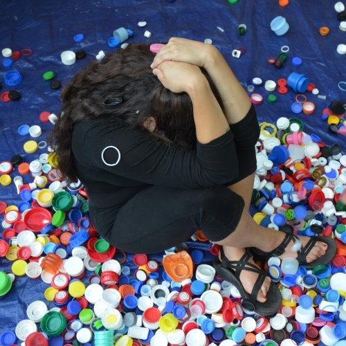 bottle caps shower down on a young woman sitting on a blue tarp during a recycling collection