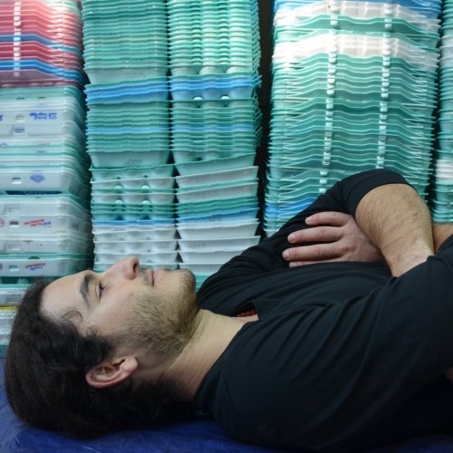 a young man supine in side profile with egg cartons stacked in the background