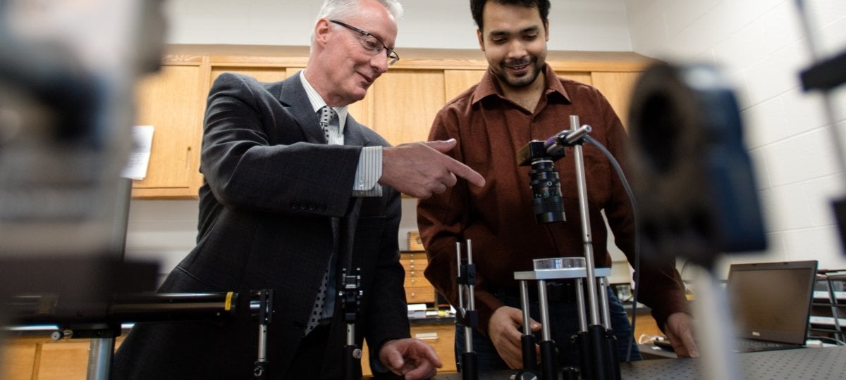 Faculty and graduate student looking over a laser