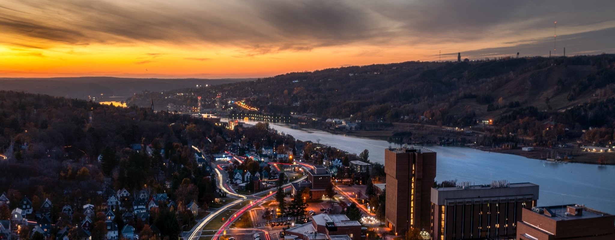 A summer sunset in Houghton, Michigan, with Michigan Tech's Campus lit by street lights and cars.
